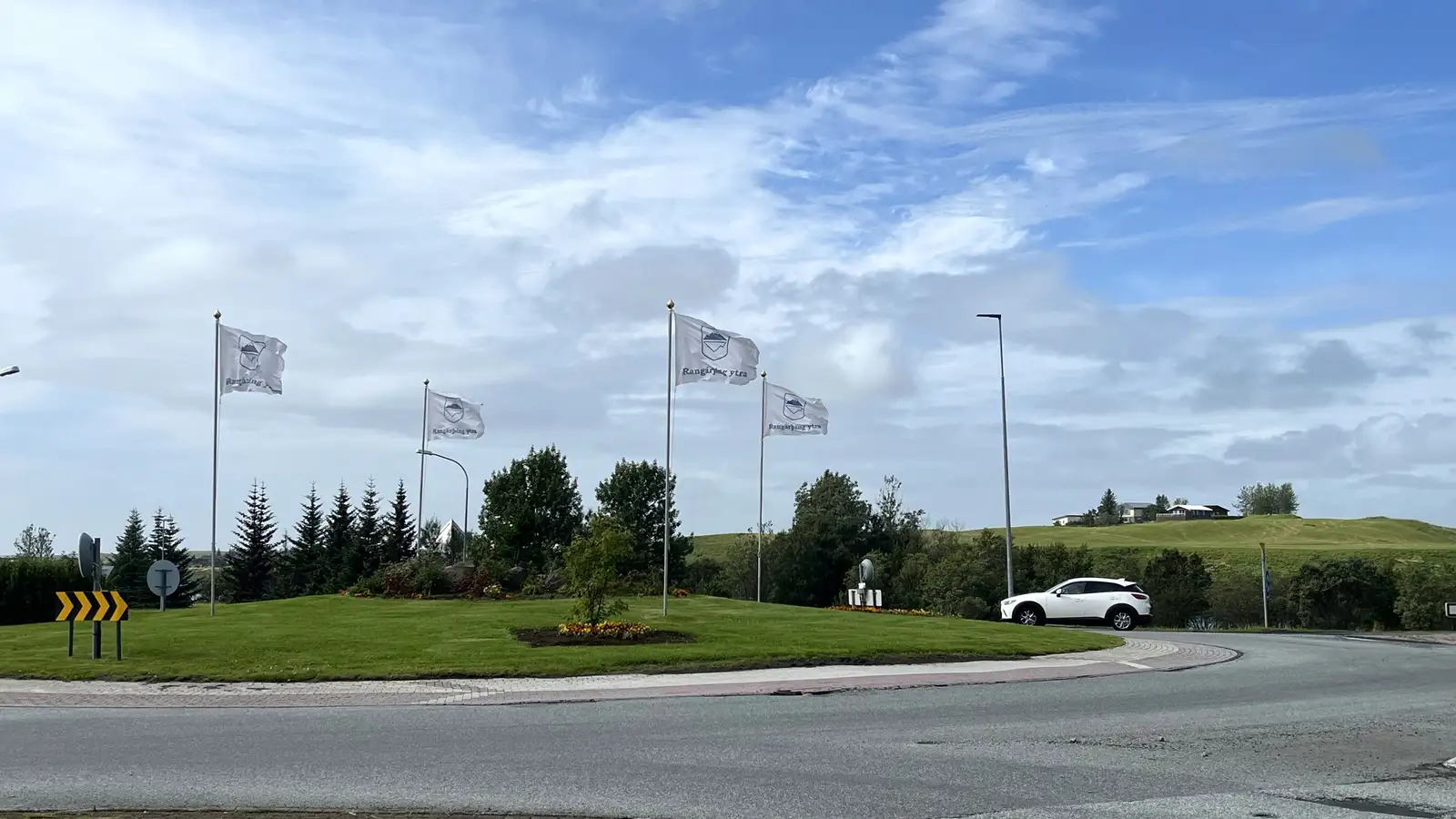 Mynd frá hringtorgi á Hellu sumarið 2024. Fánar Rangárþings ytra eru þar við hún.