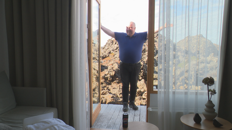 Das Foto zeigt Sigurbjörn Arnar Jónsson, einen Busfahrer, vor einem Hotelzimmer im Hotel Silica. Er breitet seine Arme aus und lächelt.