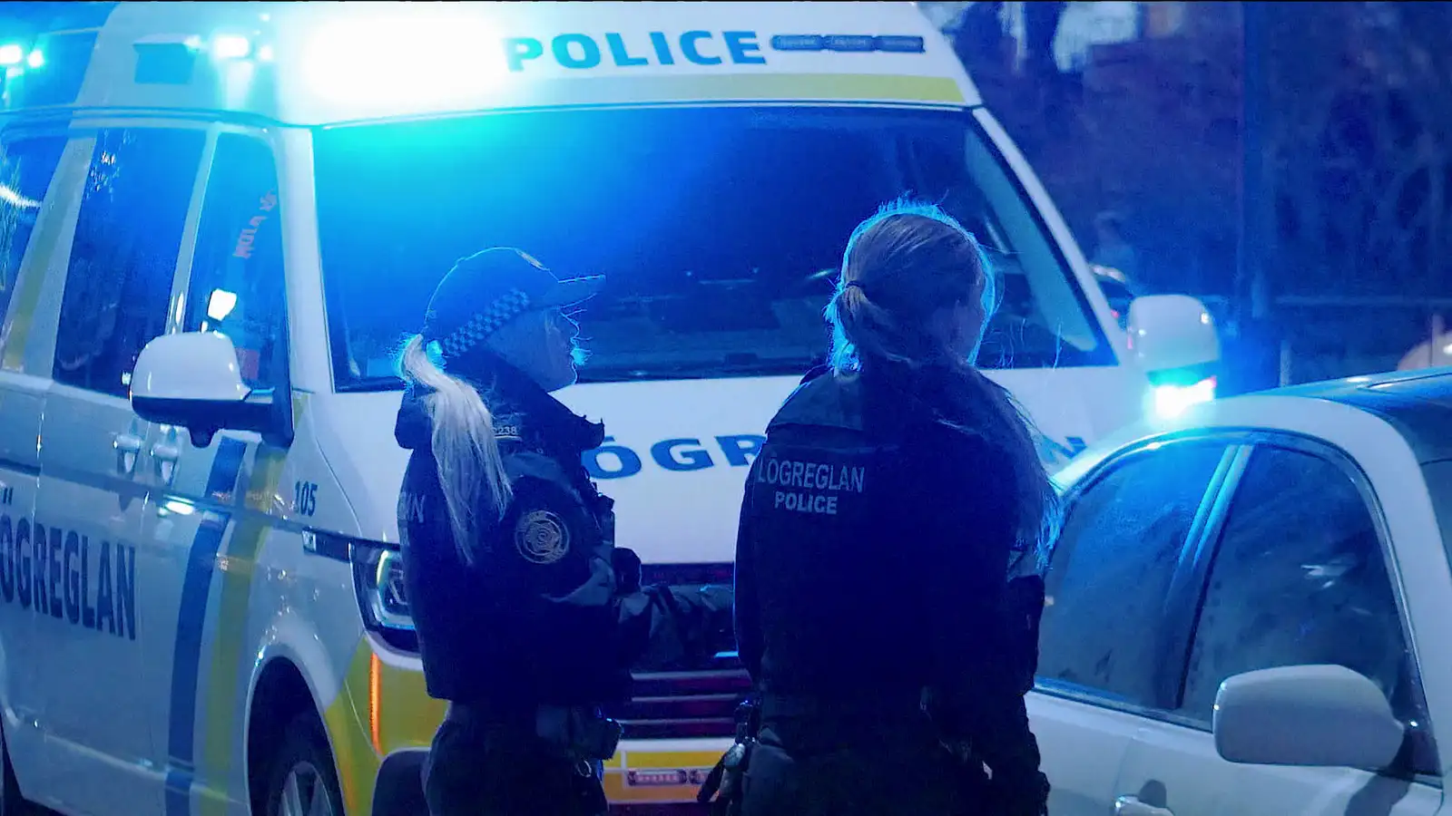 Lögreglukonur á næturvakt í miðborg Reykjavíkur, þær standa við fólksbíl. Það er stór lögreglubíll með blikkandi blá ljós fyrir aftan fólksbílinn.