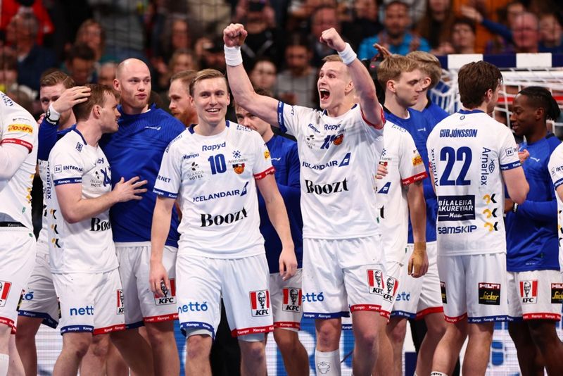Úr leik íslenska karlalandsliðsins í handbolta gegn Svartfjallalandi á EM. LEikmenn standa í hnapp á vellinum, flestir brosa. Þeir eru í hvítum búningum með bláum merkingum. Í bakgrunni má sjá áhorfendur á leiknum.