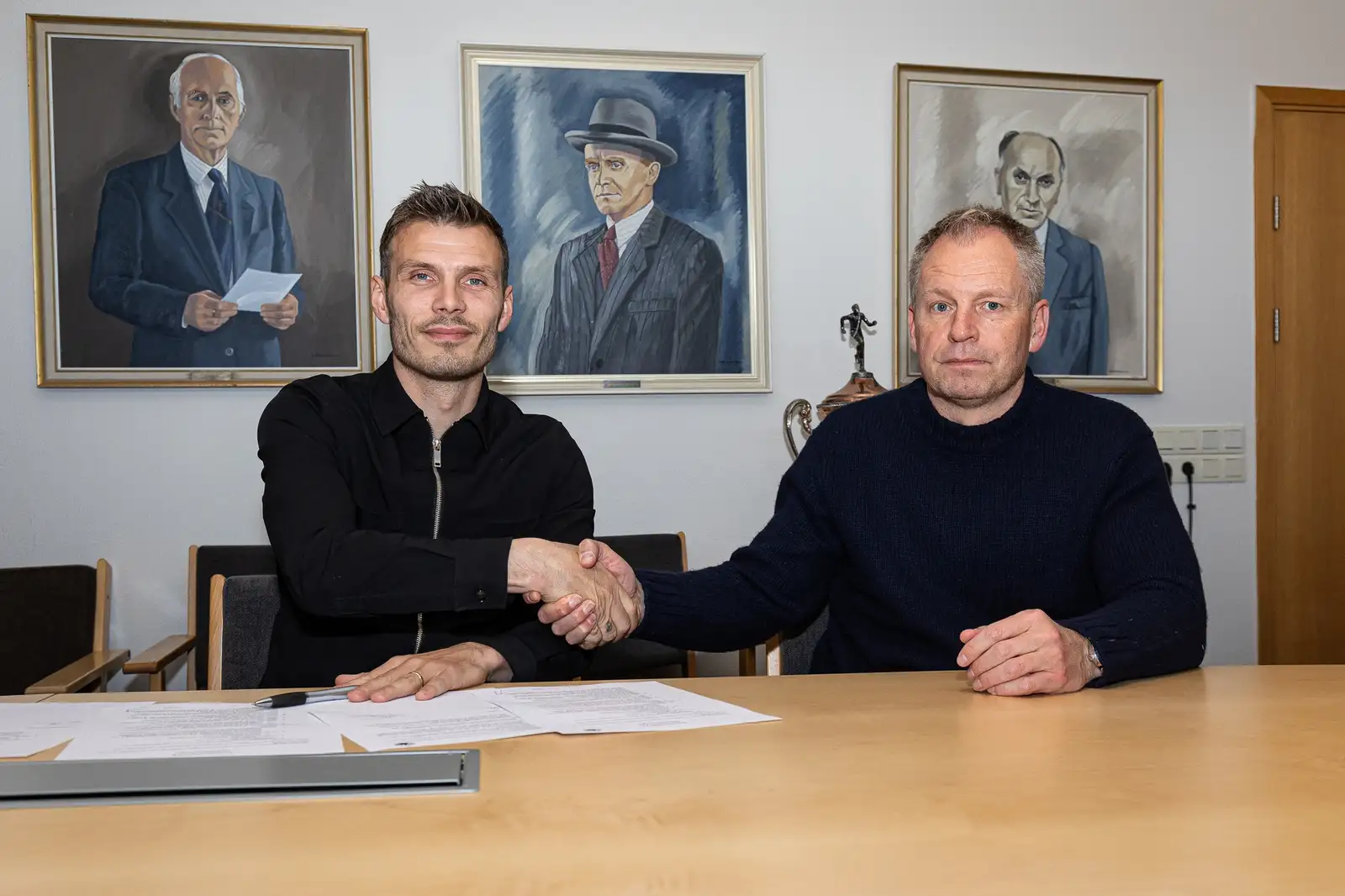 Theódor Elmar Bjarnason og Óskar Hrafn Þorvaldsson takast í hendur. Í bakgrunn sjást málverk af fyrrum formönnum KR.